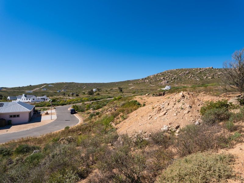 An elevated view of a vacant residential plot featuring natural rocky terrain and surrounding landscape with access to a paved road.