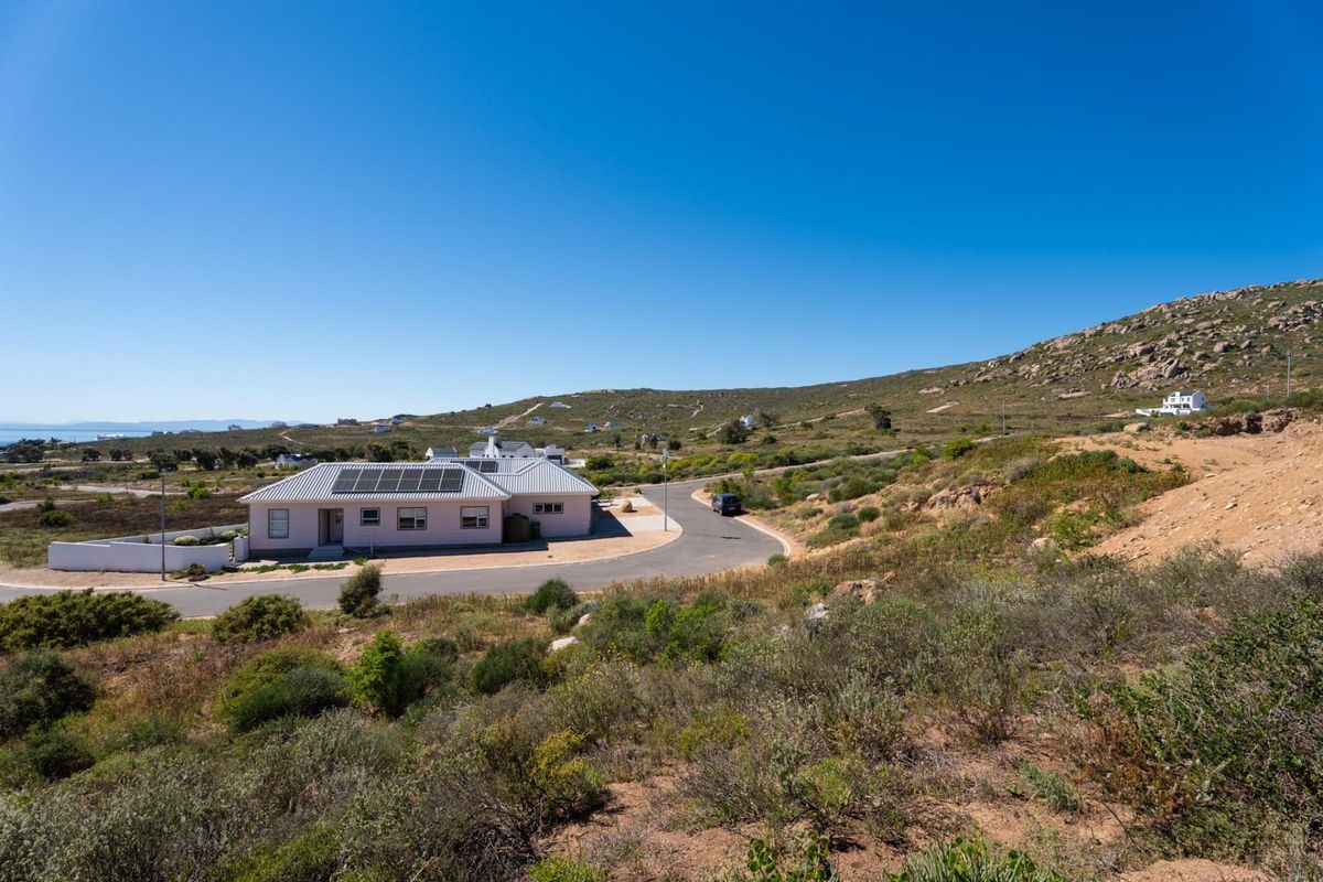 Aerial view of a residential property featuring a house with solar panels, situated in a coastal landscape with paved road access.