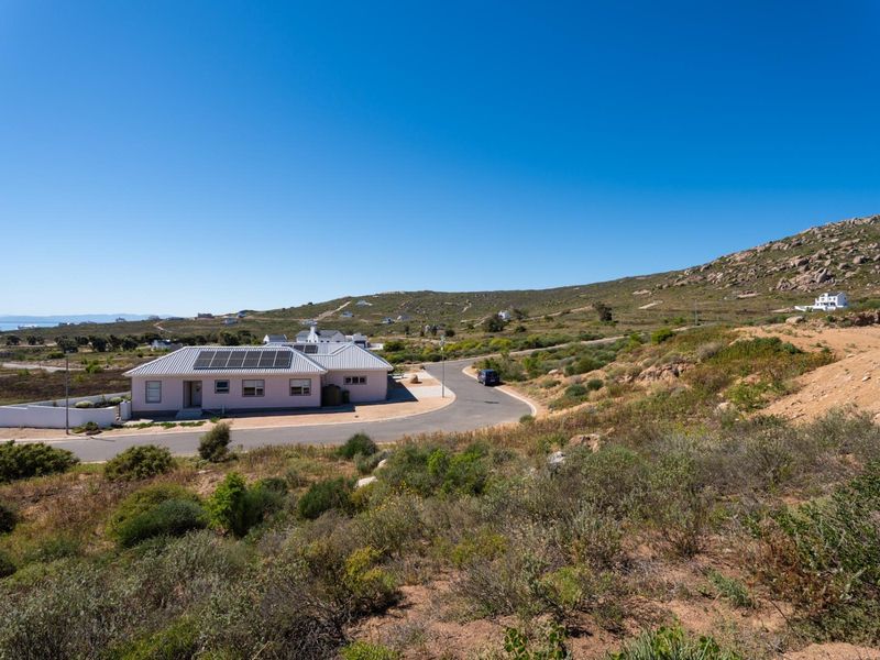 Aerial view of a residential property featuring a house with solar panels, situated in a coastal landscape with paved road access.