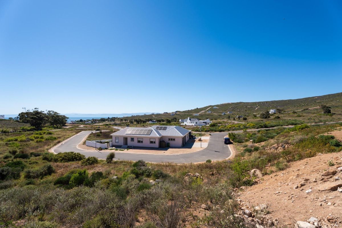 An aerial view of a residential property featuring a metal roof with solar panels, situated on a corner lot with a paved driveway.