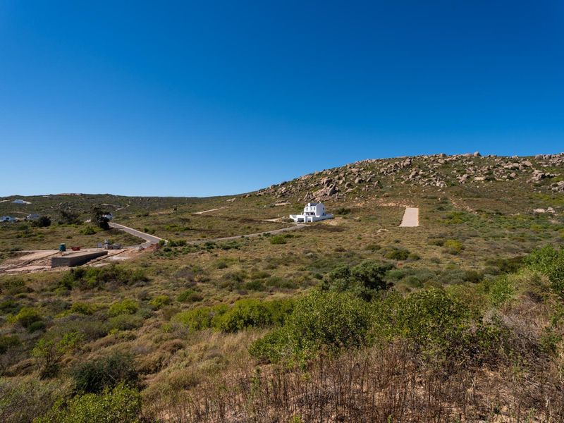 An aerial view of a large residential plot featuring natural rocky terrain, native vegetation, and established access roads within a scenic landscape.