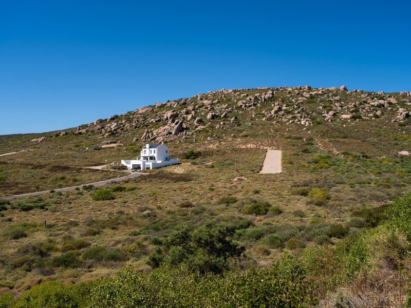 An aerial view of a residential property situated on a large, hilly plot of land with natural vegetation and a paved driveway.