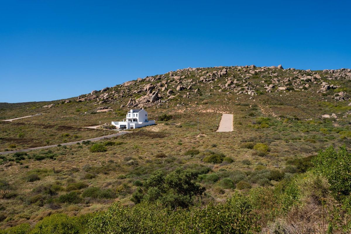 An aerial view of a residential property situated on a large, hilly plot of land with natural vegetation and a paved driveway.