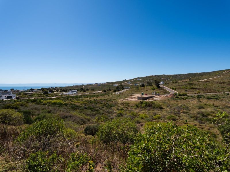 A wide-angle view of the vacant residential land, showcasing the surrounding coastal landscape, natural vegetation, and nearby road infrastructure.
