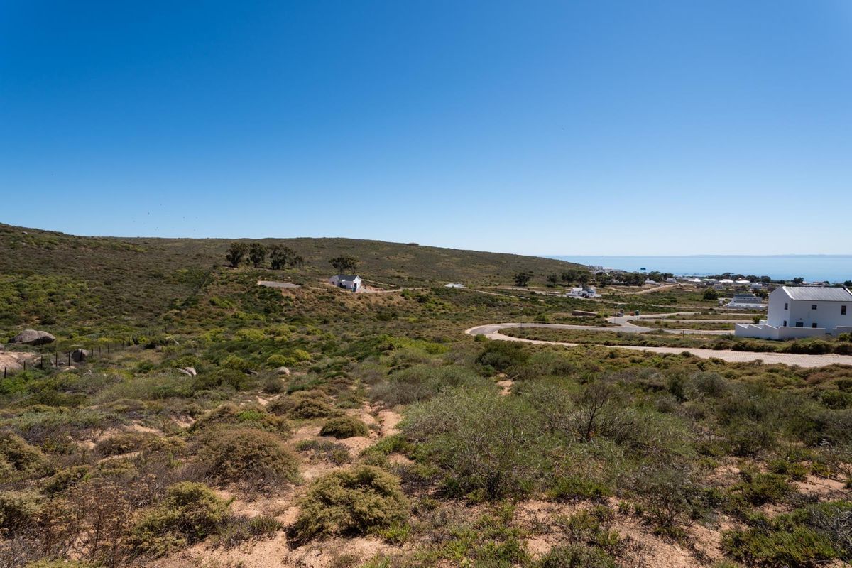 A scenic elevated view of the coastal landscape, featuring natural vegetation, rolling hills, and nearby residential development with paved access roads.