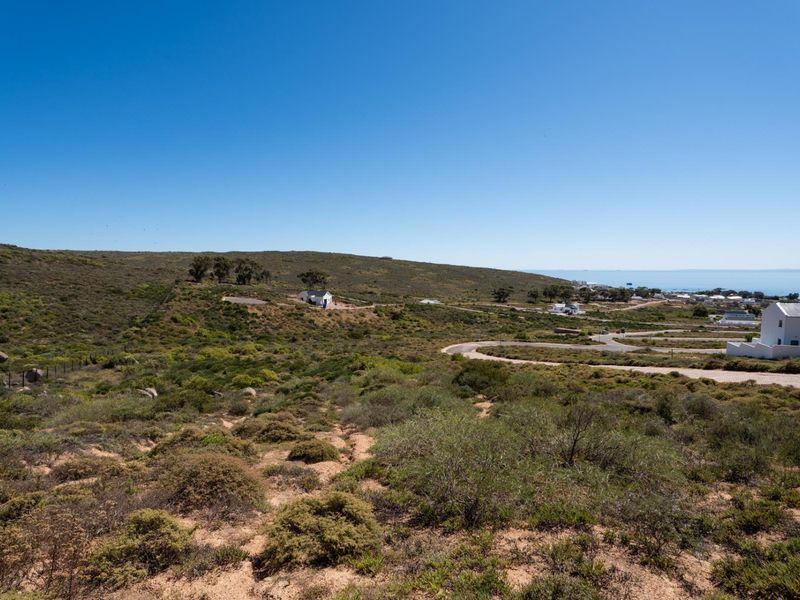 A scenic elevated view of the coastal landscape, featuring natural vegetation, rolling hills, and nearby residential development with paved access roads.