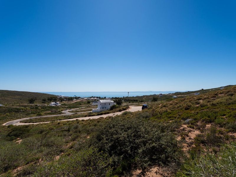 A wide-angle view of the coastal landscape and surrounding residential area, showcasing the natural terrain and access roads leading to the property.