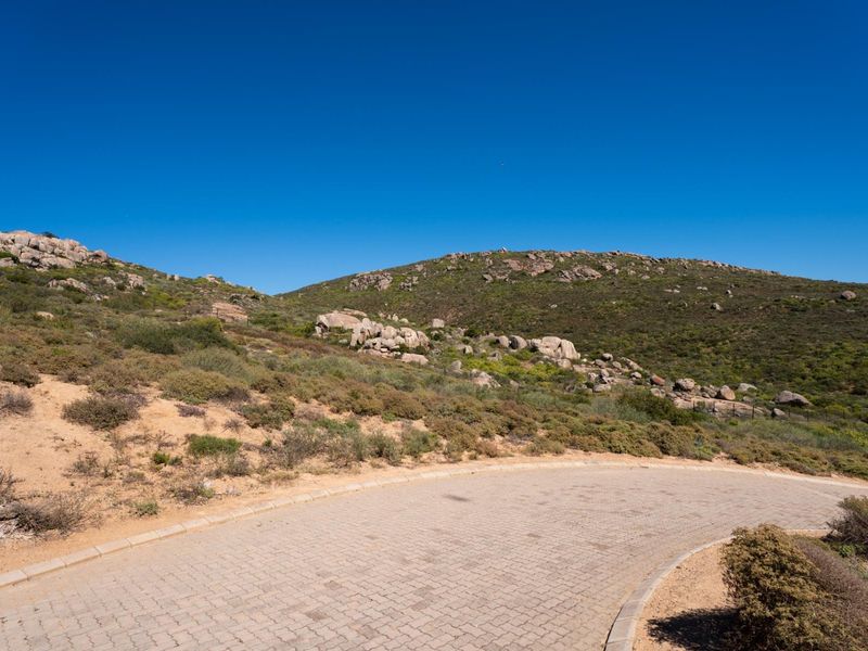 A view of a paved residential driveway leading into a natural, rocky hillside landscape under a clear blue sky.