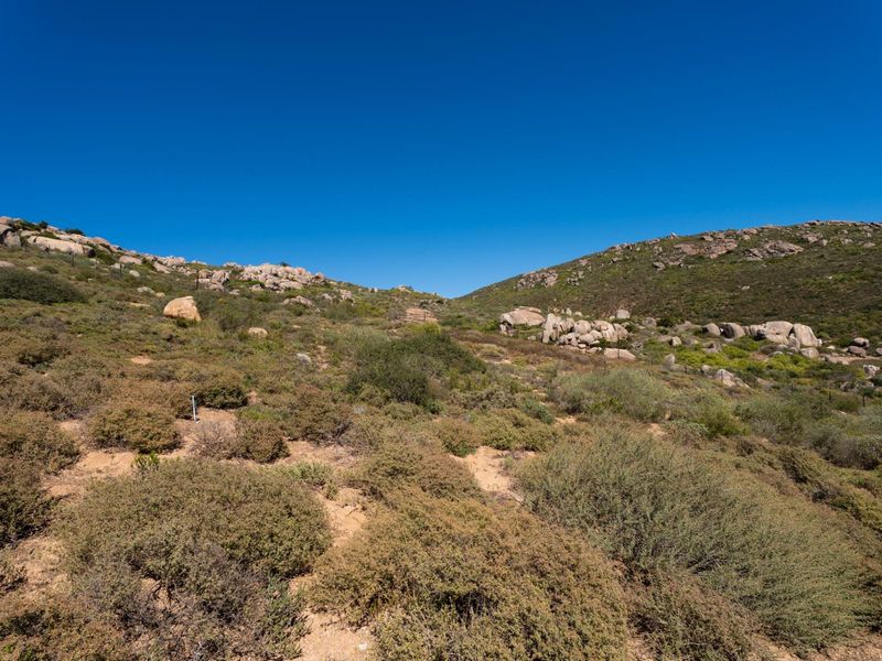 A scenic view of the vacant residential land featuring natural rock formations and native hillside vegetation under a clear blue sky.