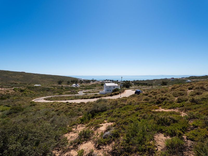 A scenic elevated view of the surrounding coastal landscape, featuring natural vegetation and a paved access road leading through the residential area.
