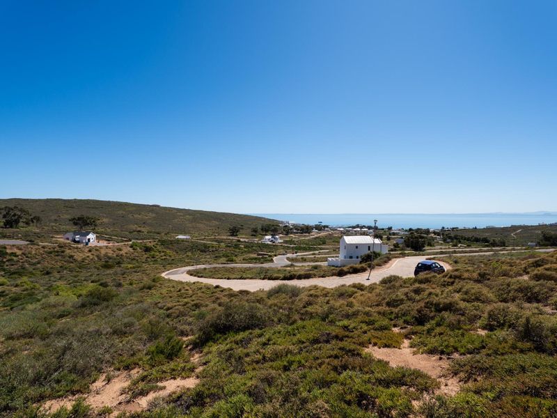 A scenic elevated view of the coastal residential estate, showcasing the natural landscape, winding access roads, and distant ocean horizon.