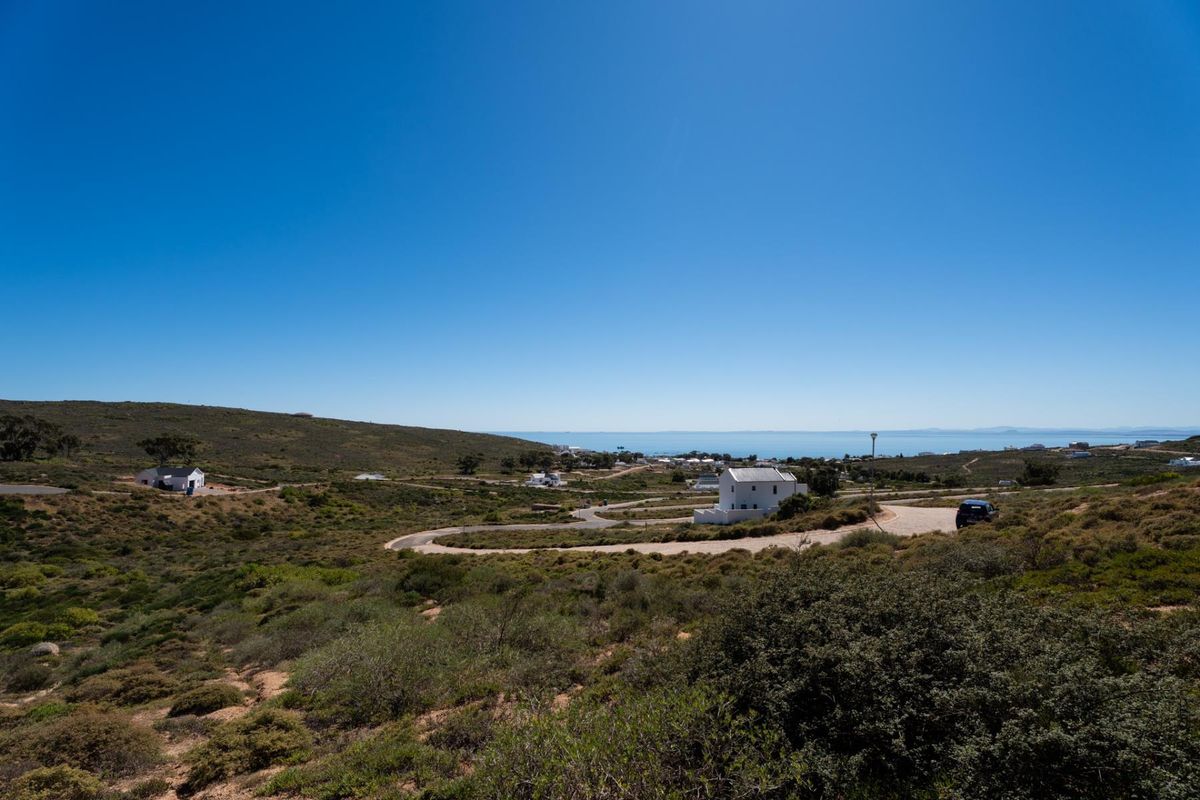 An elevated aerial view of a residential development area featuring winding paved roads, natural coastal vegetation, and distant ocean views.
