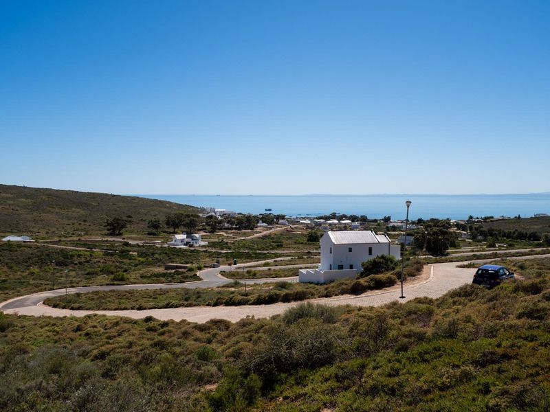 A scenic elevated view of the coastal residential estate, featuring natural landscape, paved roads, and distant ocean vistas.