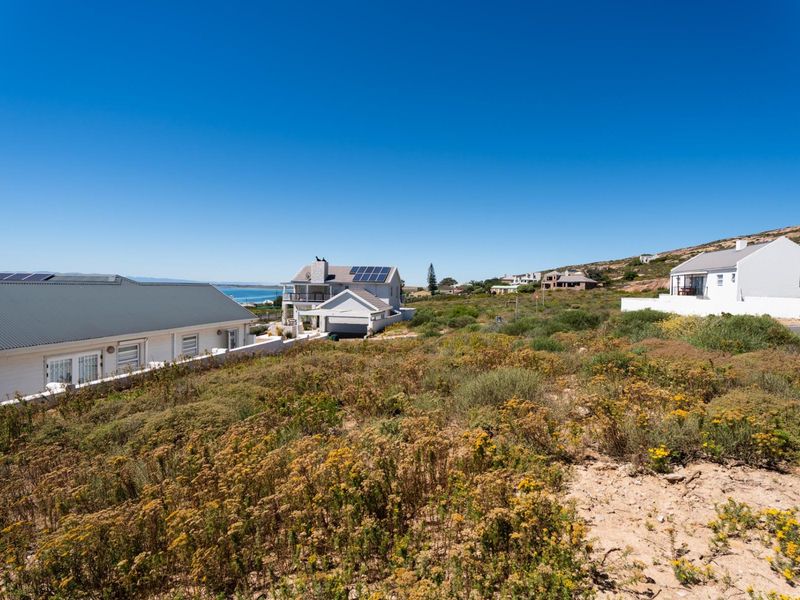 A view of a vacant residential plot featuring natural coastal vegetation with surrounding established homes in a quiet neighborhood.
