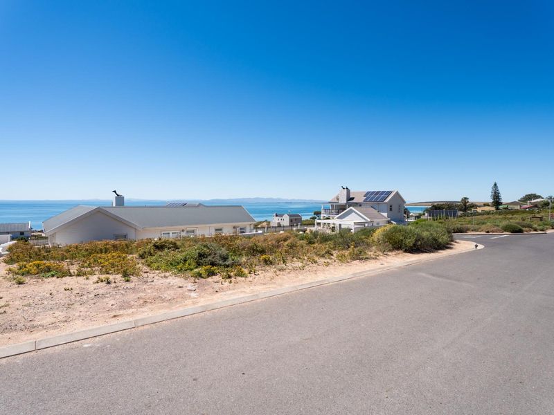 A clear street-level view of the residential plot featuring coastal surroundings and established neighborhood infrastructure under a bright blue sky.