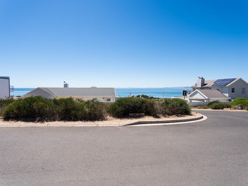 A clear street view of the residential area, showcasing the paved road, curb infrastructure, and surrounding coastal landscape.