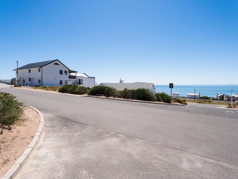 A clear street view of the residential area showing the paved road, curbing, and surrounding coastal landscape.
