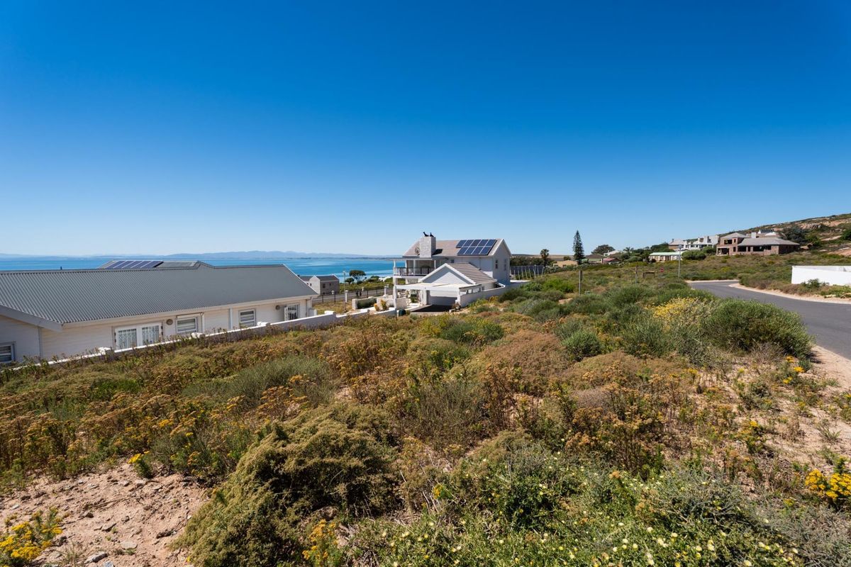 A scenic view of a coastal residential area featuring natural vegetation, nearby homes, and a clear view of the ocean.