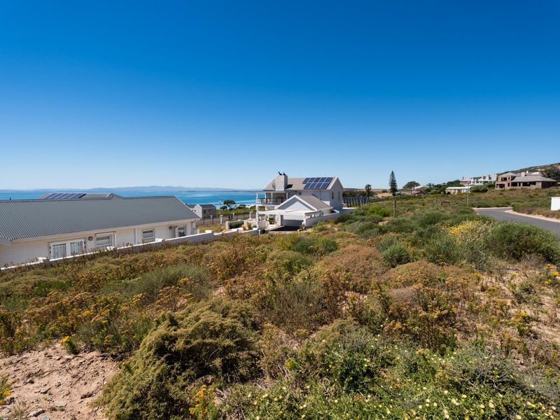 A scenic view of a coastal residential area featuring natural vegetation, nearby homes, and a clear view of the ocean.
