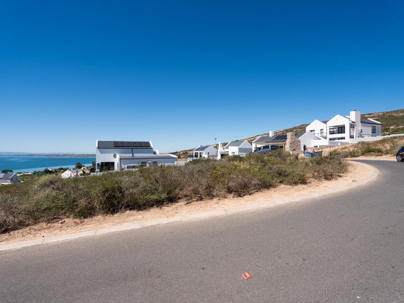 A street-level view of a coastal residential development featuring modern homes with solar panels, overlooking the ocean.