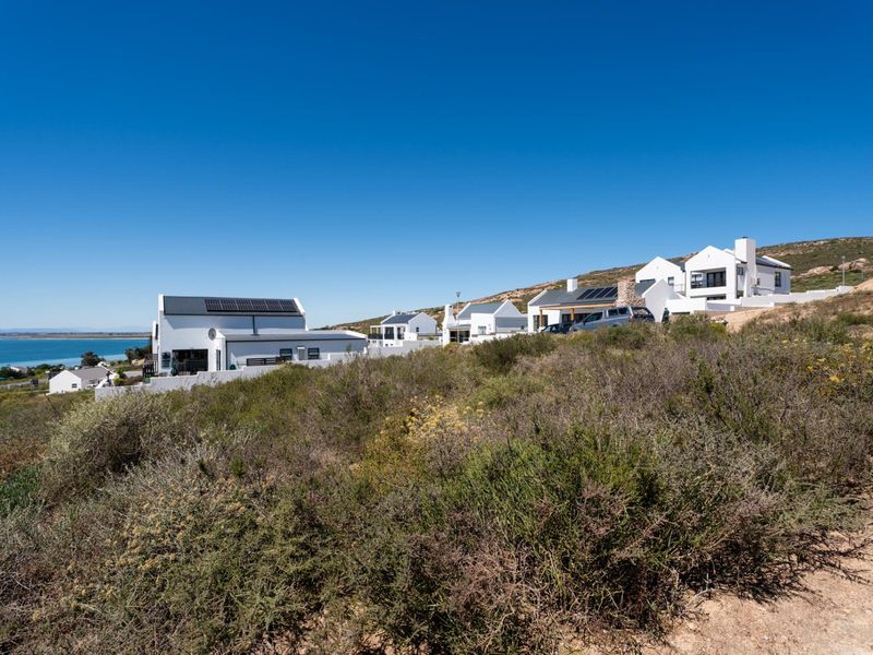 A scenic elevated view of a coastal residential estate featuring white modern homes set against a natural landscape and ocean backdrop.