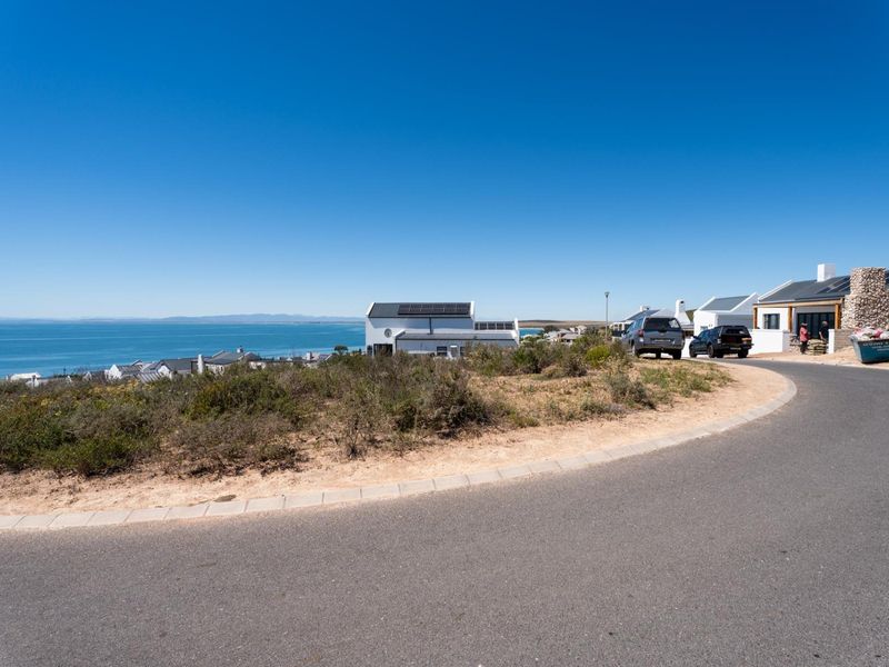 A street-level view of a residential area featuring paved roads, coastal surroundings, and distant ocean views.