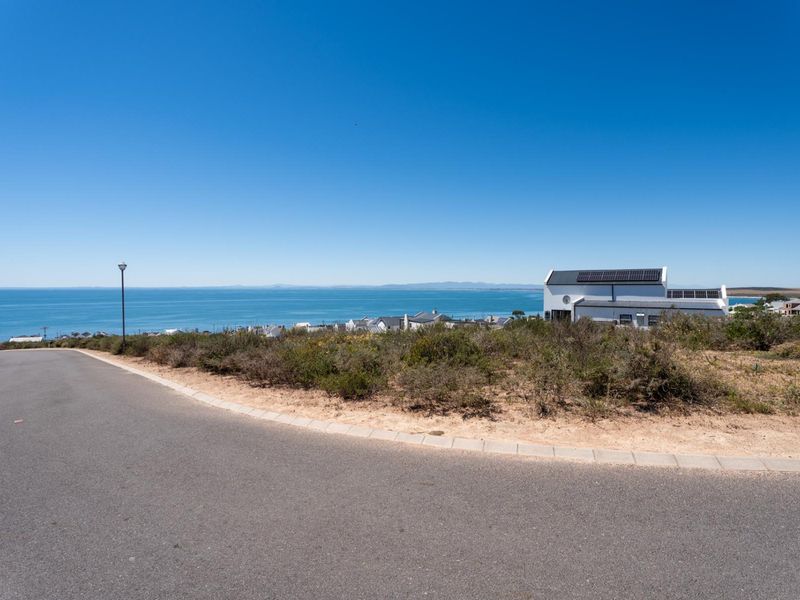 A scenic view of the ocean and coastline from a paved residential street, showcasing the coastal location and surrounding landscape.