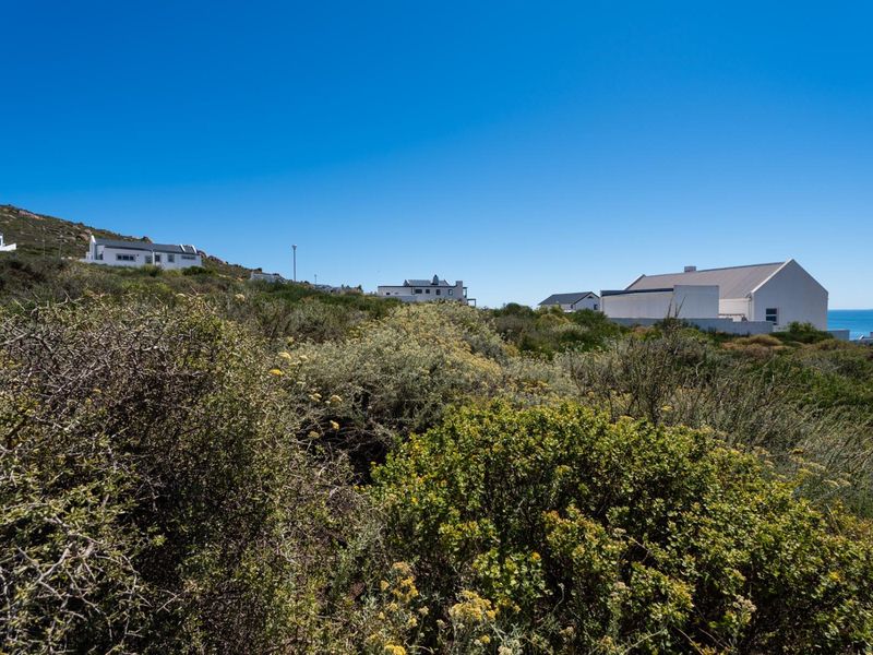 A view of the vacant residential land featuring natural coastal vegetation and a sloped landscape with neighboring properties visible in the background.