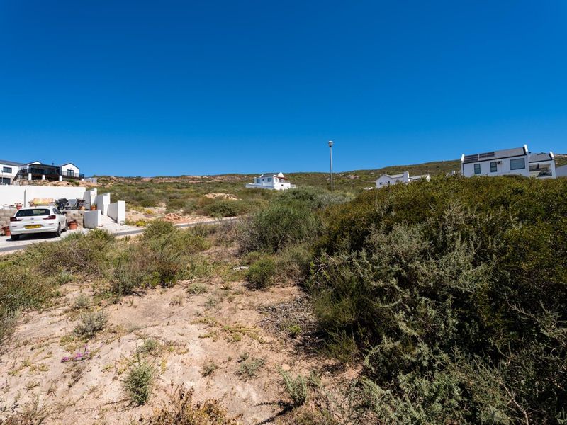 A view of a vacant residential plot featuring native vegetation, situated in a developed coastal neighborhood with surrounding residential properties.