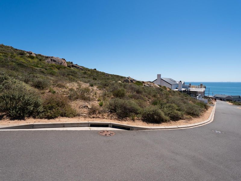 A street-level view of the vacant residential land, featuring established asphalt road infrastructure, concrete curbing, and coastal landscape views.