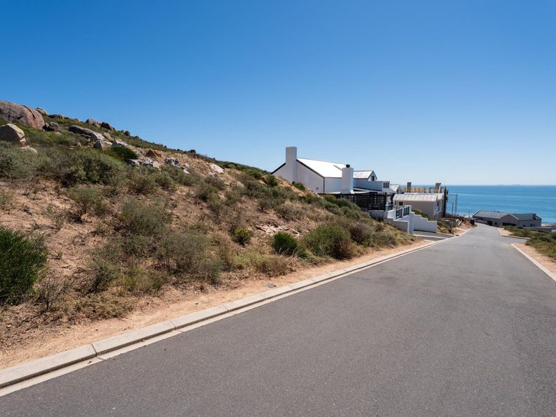 A view of the paved street and sloped residential land with coastal views in the background.