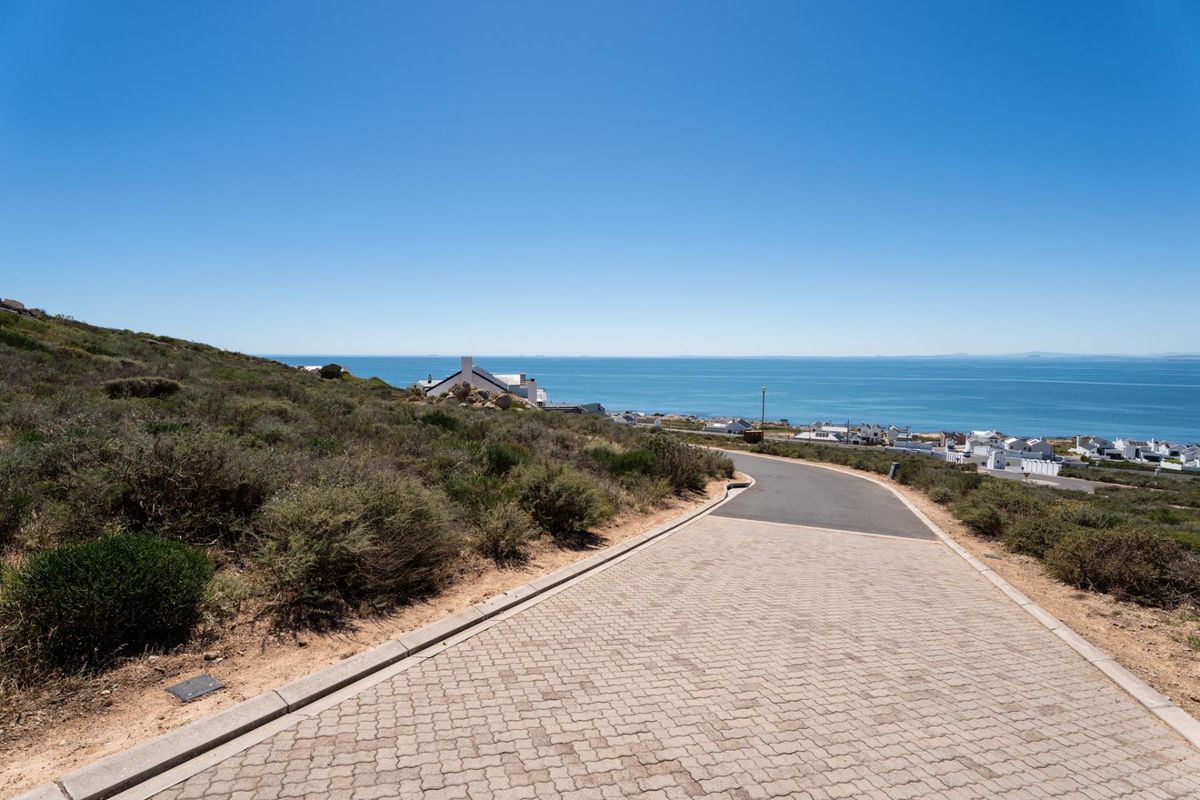 A view of a paved residential street leading towards the coastline, showcasing the surrounding landscape and coastal proximity.