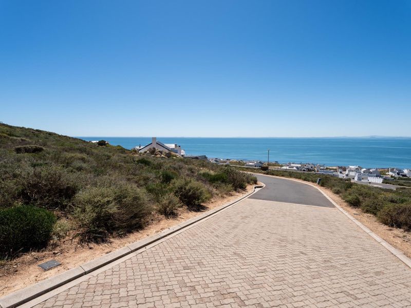 A view of a paved residential street leading towards the coastline, showcasing the surrounding landscape and coastal proximity.