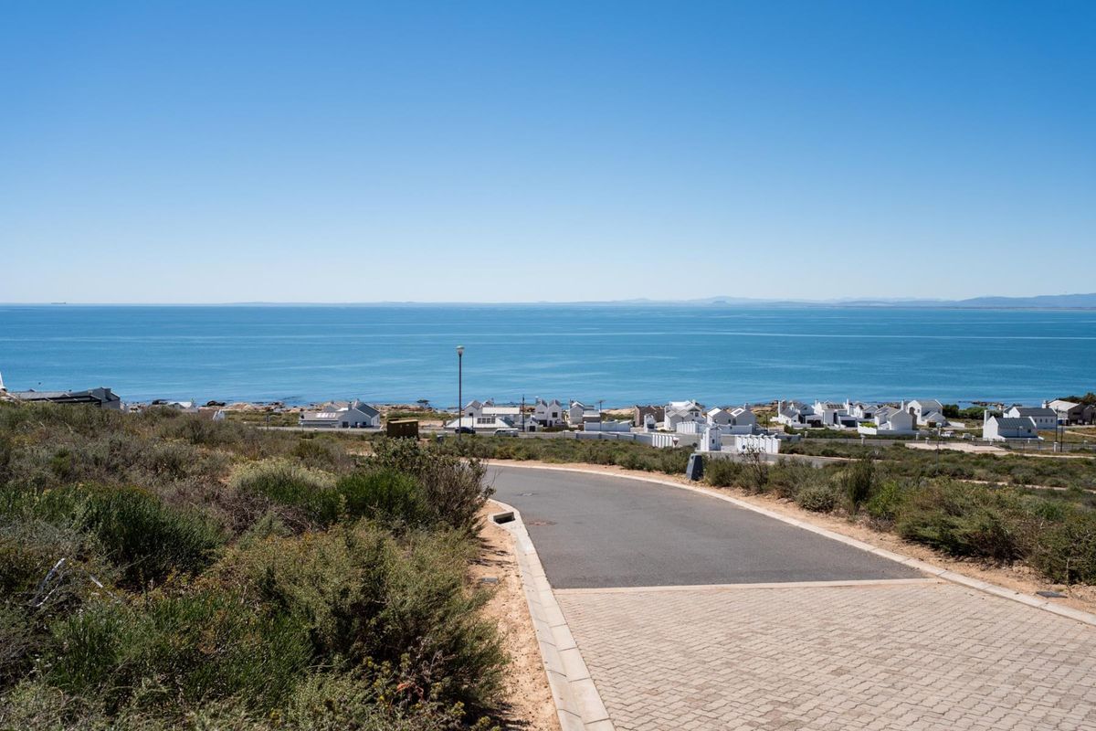 A scenic view overlooking the ocean and coastal residential area, featuring a paved driveway leading towards the horizon.