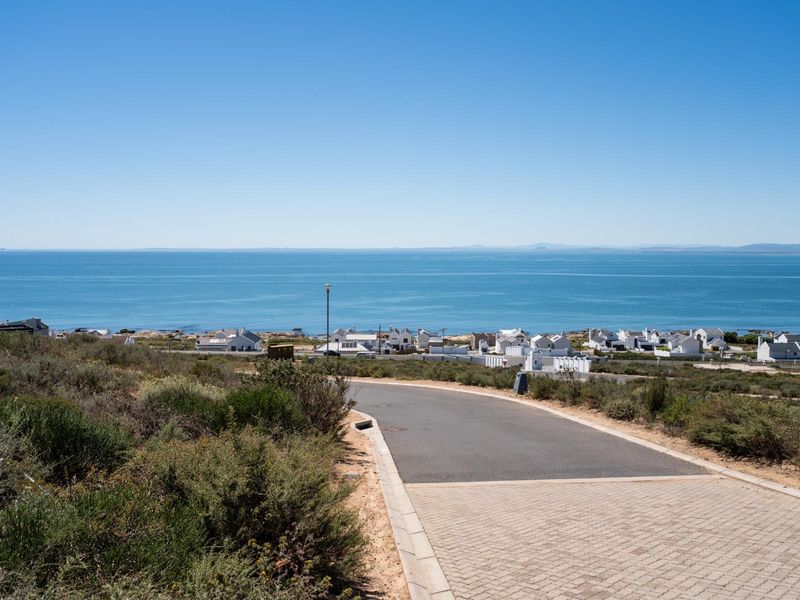 A scenic view overlooking the ocean and coastal residential area, featuring a paved driveway leading towards the horizon.