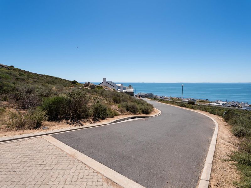 A view of the paved residential street leading towards the coastline, showcasing the surrounding natural landscape and coastal setting.