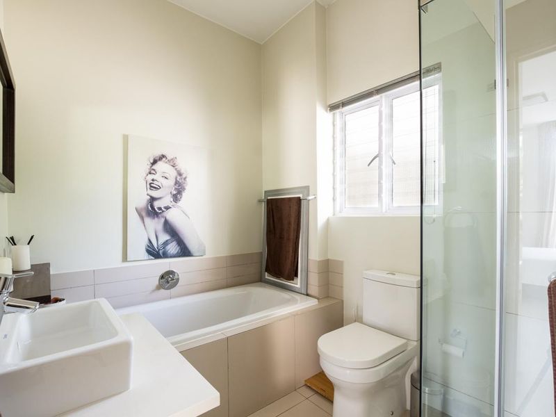 A modern, well-maintained bathroom featuring a built-in bathtub, a separate glass-enclosed shower, a contemporary basin, and neutral tiling.