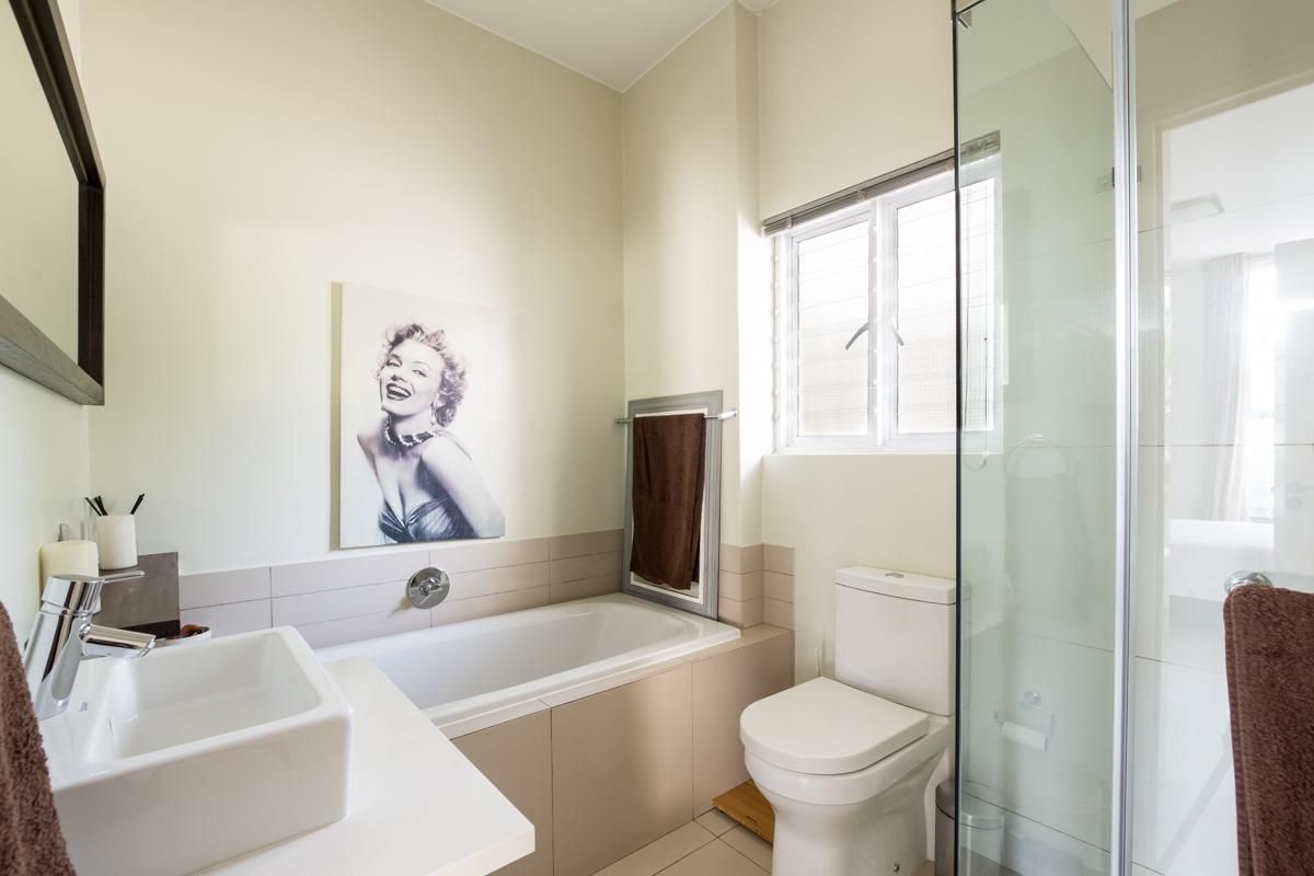 A modern, well-maintained bathroom featuring a built-in bathtub, a separate glass-enclosed shower, a contemporary basin, and neutral tiling.