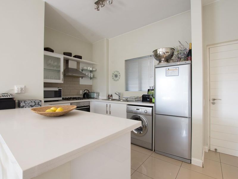 A modern, well-maintained kitchen featuring quartz countertops, built-in cabinetry, a gas hob, and integrated stainless steel appliances with tiled flooring.