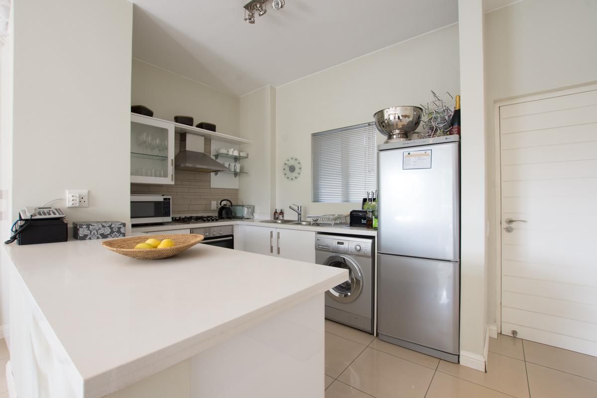 A modern, well-maintained kitchen featuring quartz countertops, built-in cabinetry, a gas hob, and integrated stainless steel appliances with tiled flooring.