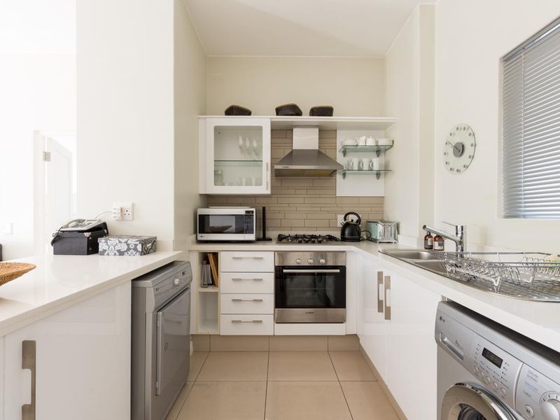 Modern compact kitchen featuring white cabinetry, stone countertops, built-in oven, gas hob, extractor fan, and integrated laundry appliance space.