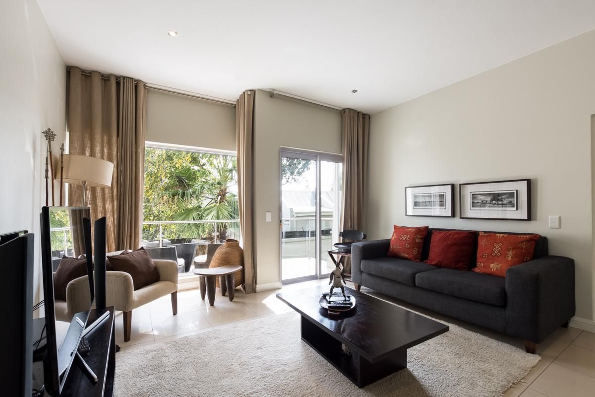 A bright and well-maintained living room featuring tiled floors, recessed lighting, and large sliding glass doors that provide access to an outdoor balcony.