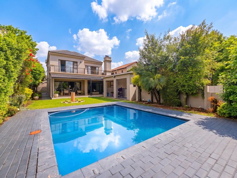 A well-maintained rear garden featuring a swimming pool, paved deck, covered patio area, and a two-story residential building with a balcony.