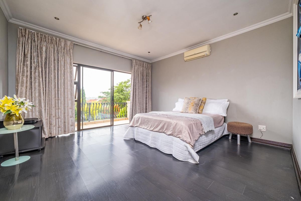 Spacious bedroom featuring dark laminate flooring, wall-mounted air conditioning, and sliding glass doors leading to a private balcony.