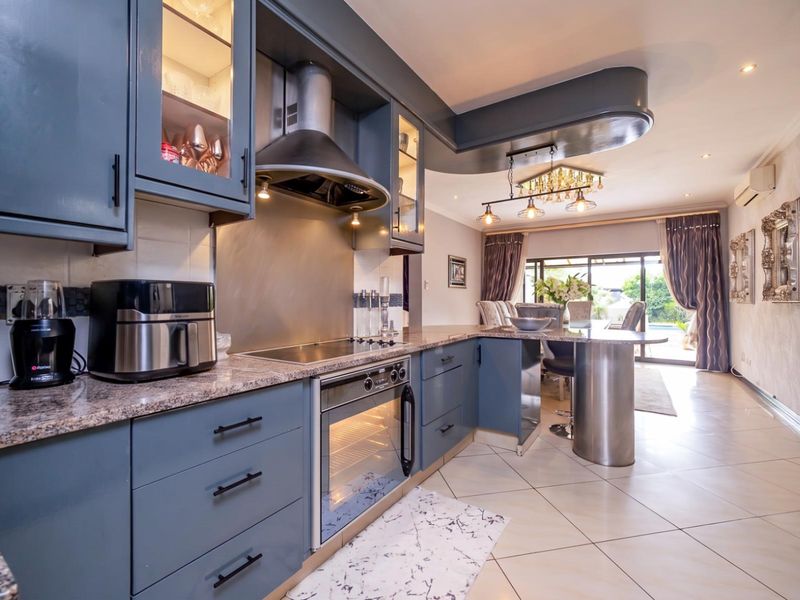 Modern open-plan kitchen featuring blue cabinetry, granite countertops, integrated appliances, and a breakfast bar, flowing seamlessly into the dining and living area.