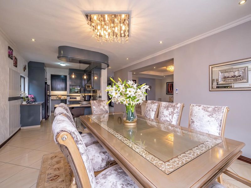Spacious open-plan dining and kitchen area featuring modern cabinetry, a central island, elegant lighting fixtures, and polished tiled flooring throughout.