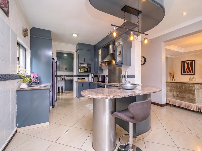 Modern kitchen featuring dark cabinetry, granite countertops, a central breakfast bar, and integrated stainless steel appliances, flowing into an open-plan living area.