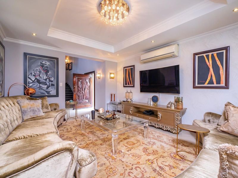 Elegant living room featuring a recessed ceiling with a chandelier, wall-mounted air conditioning, and a decorative carved wooden entrance door.