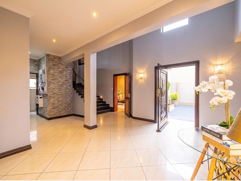 Spacious entrance hall featuring polished tiled flooring, a stone-clad feature wall, and a staircase leading to the upper level.