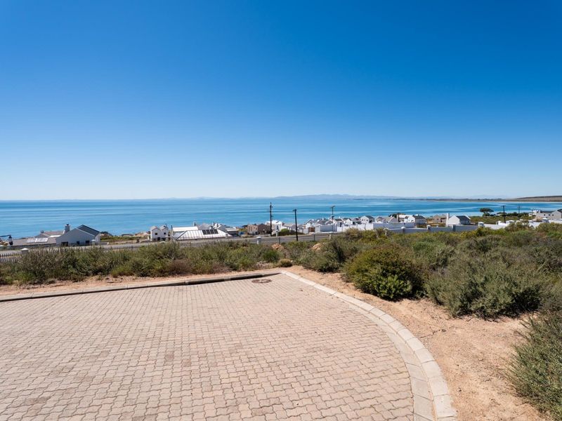 A vacant residential plot featuring a paved driveway area with expansive, unobstructed ocean and coastal views.